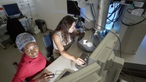 Two female chemists working on an electron microscope.